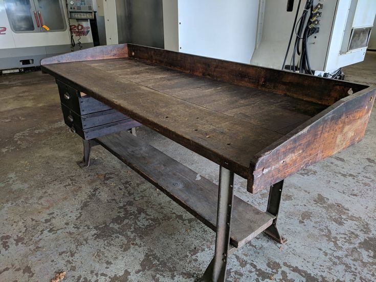 an old wooden table with metal legs in a garage area next to a white wall