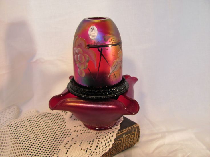 a colorful glass vase sitting on top of a book next to a lace doily