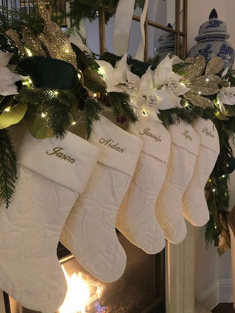 christmas stockings hanging from a mantel decorated with greenery and white poinsettis