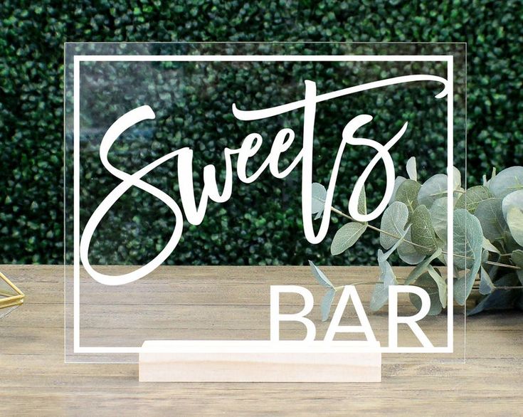 a wooden table topped with a vase filled with flowers and greenery next to a sign that says sweet's bar