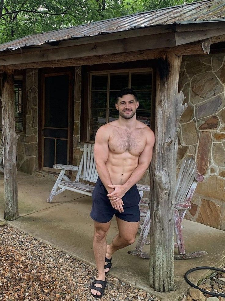 a shirtless man standing in front of a stone building