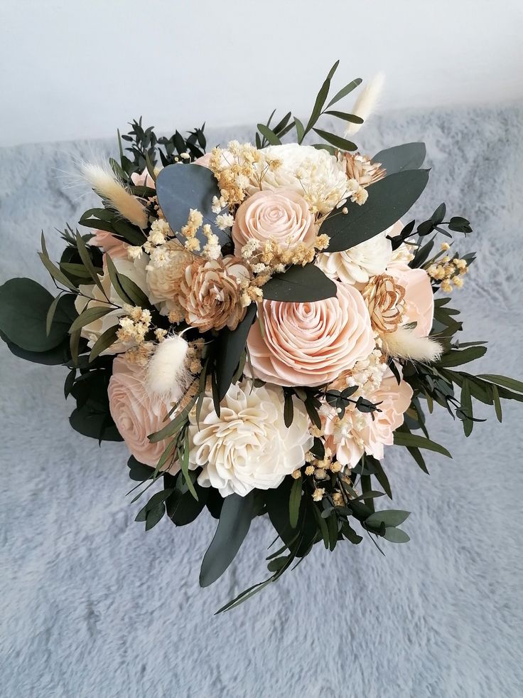 a bridal bouquet with peach and white flowers on a gray blanketed surface in the background