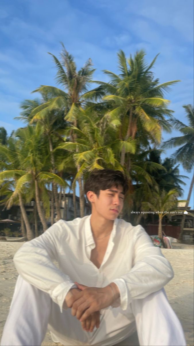 a man sitting on top of a sandy beach next to palm trees