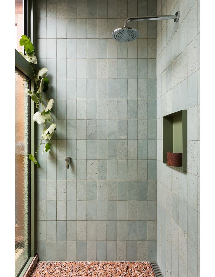 a shower with green tile and pink pebbles on the floor next to it is an open window