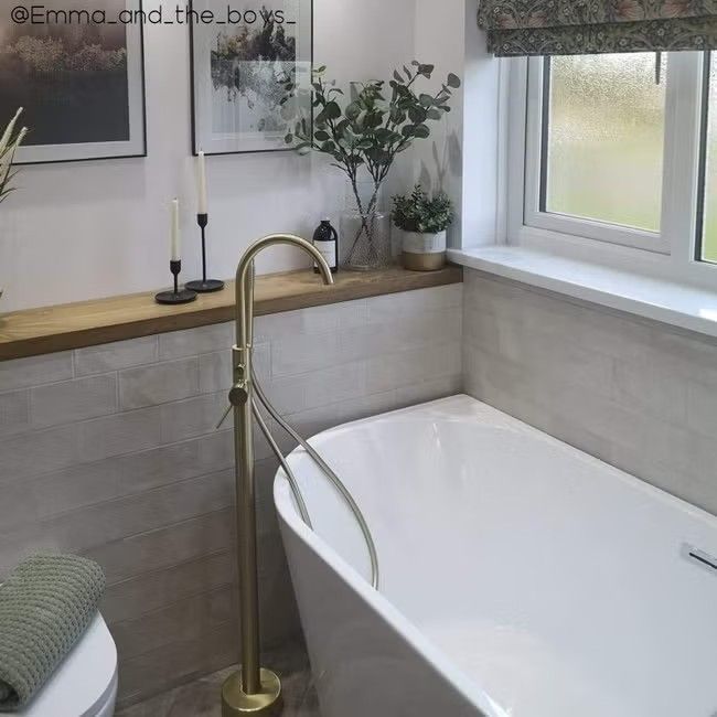 a white bath tub sitting next to a toilet under a window with two pictures on the wall