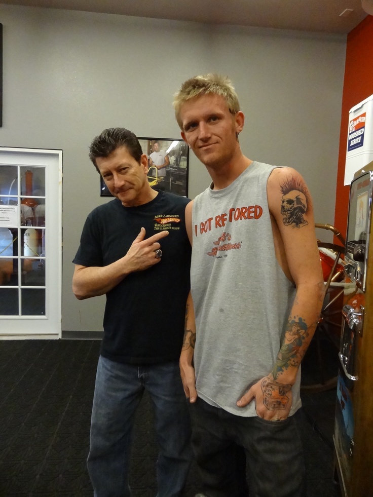 two men standing next to each other with tattoos on their arms and shoulder, both looking at the camera