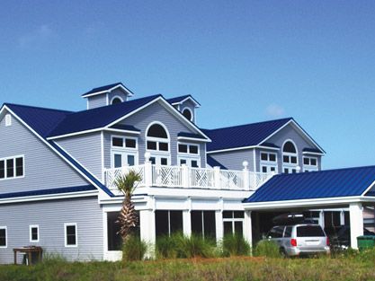 a car parked in front of a large gray house with blue roof and white balconies