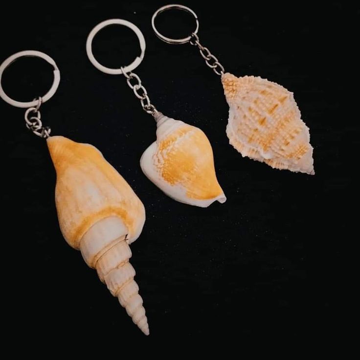 three seashells are hanging from key chains on a black surface, one is yellow and the other is white