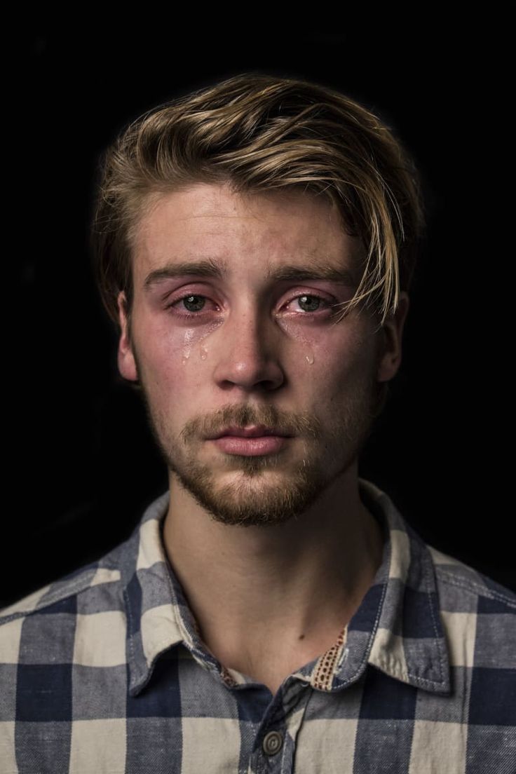 a young man with tears on his face is posing for a photo in front of a black background