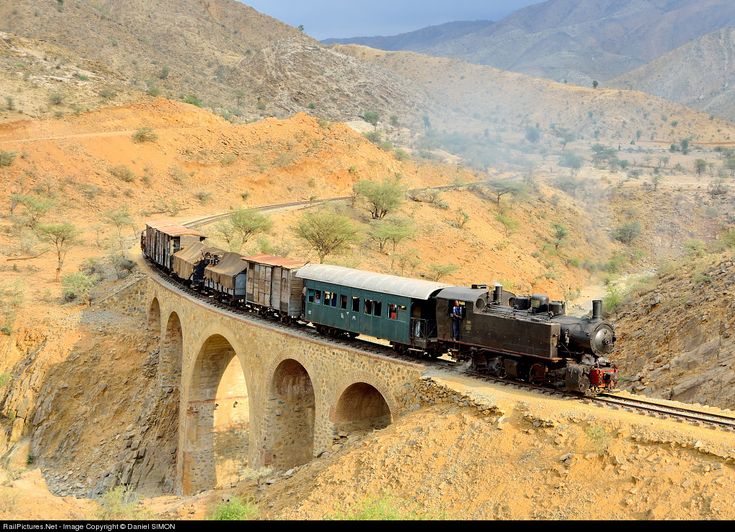 a train traveling over a bridge on top of a dirt hill next to a mountain