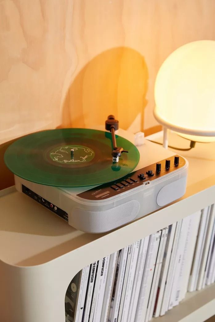 a record player sitting on top of a white shelf next to a lamp and bookshelf