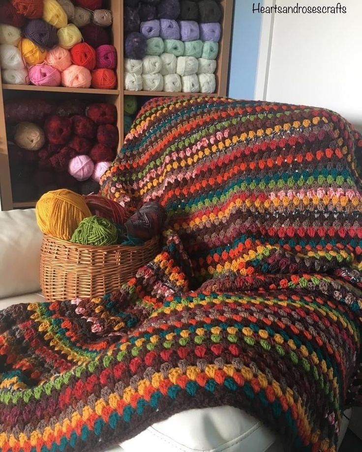 a crocheted blanket sitting on top of a couch next to a basket filled with balls of yarn