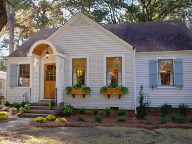 a white house with blue shutters and flowers on the front door, along with steps leading up to it