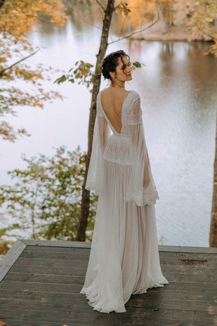 a woman in a wedding dress standing on a deck next to trees looking at the water