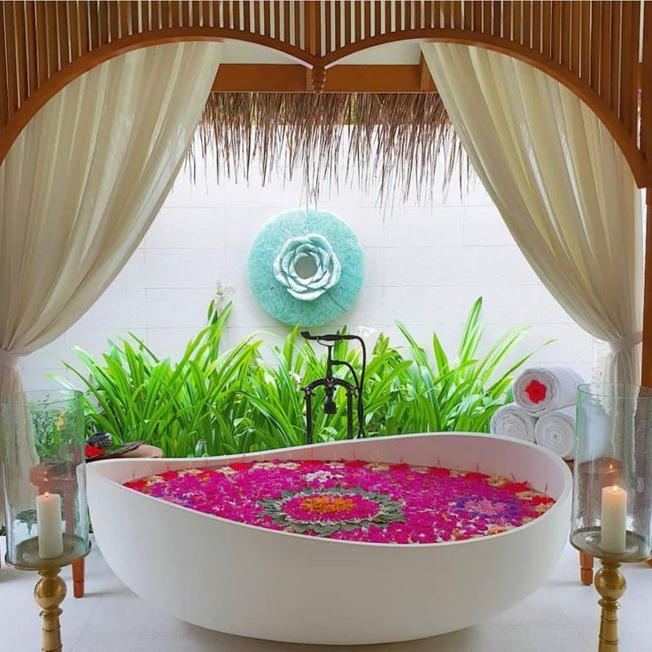 a large bath tub sitting in the middle of a room next to plants and candles