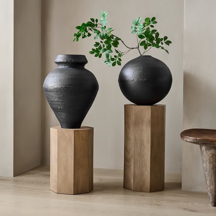 two black vases sitting on top of wooden blocks next to each other with a plant in them