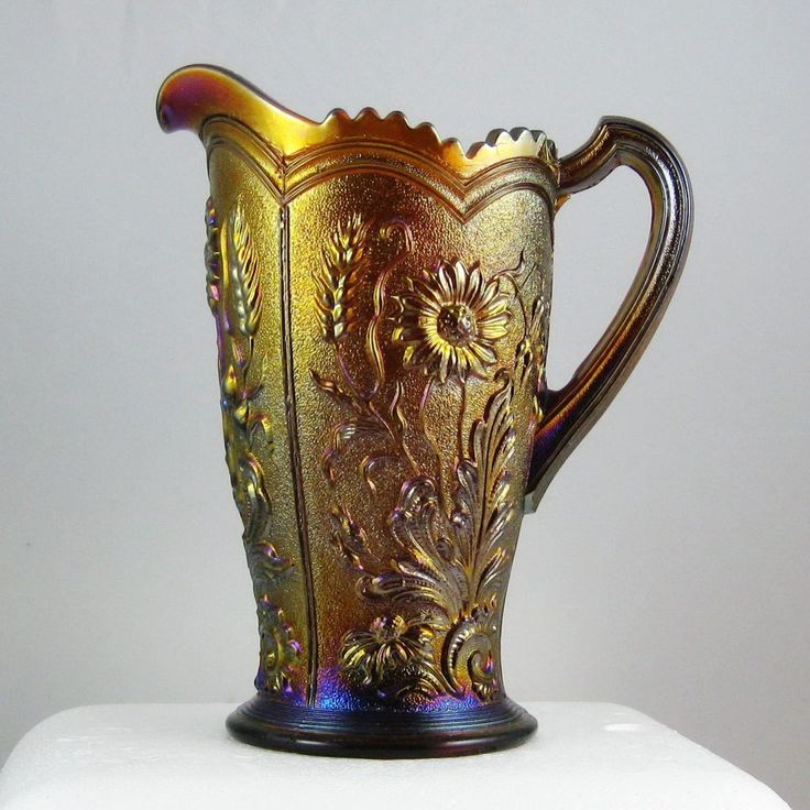 an ornate glass pitcher is sitting on top of a white surface, with gold trimmings