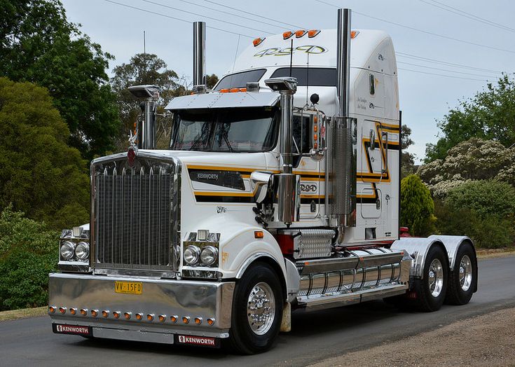 a large semi truck driving down a road next to some trees and bushes on either side of the road