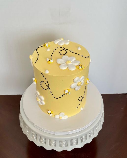 a yellow and white cake with flowers on it sitting on top of a wooden table