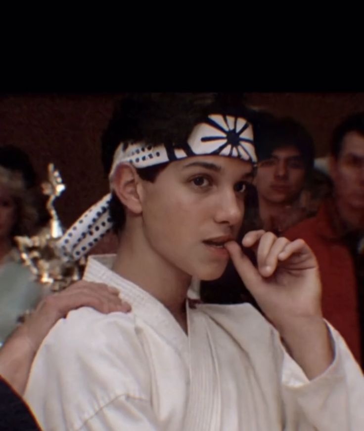 a man in karate attire talking on a cell phone while others look on from behind him