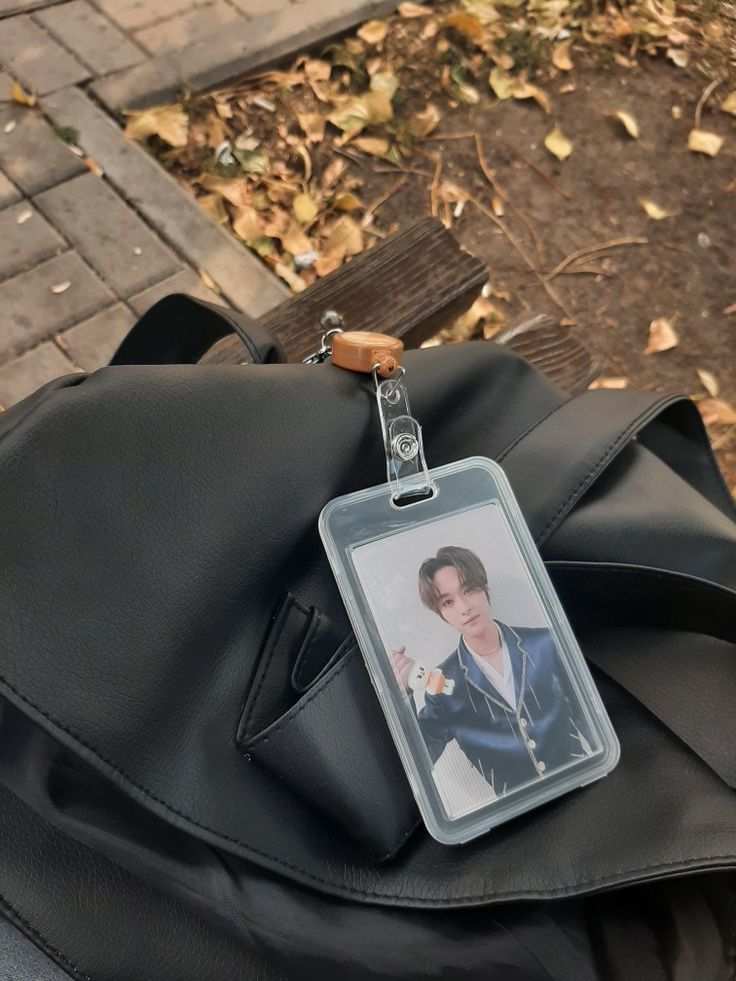 an id card attached to a backpack on the ground with leaves around it and a sidewalk in the background