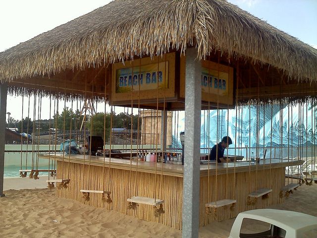 a tiki bar on the beach with thatched roof and people sitting at it