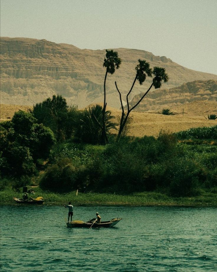 two people in a small boat on the water with mountains in the backgroud