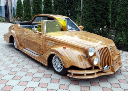 a car made out of wood sitting on top of a brick floor next to trees