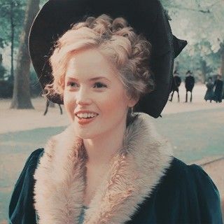 a woman wearing a black hat and fur collar smiling at the camera with other people in the background