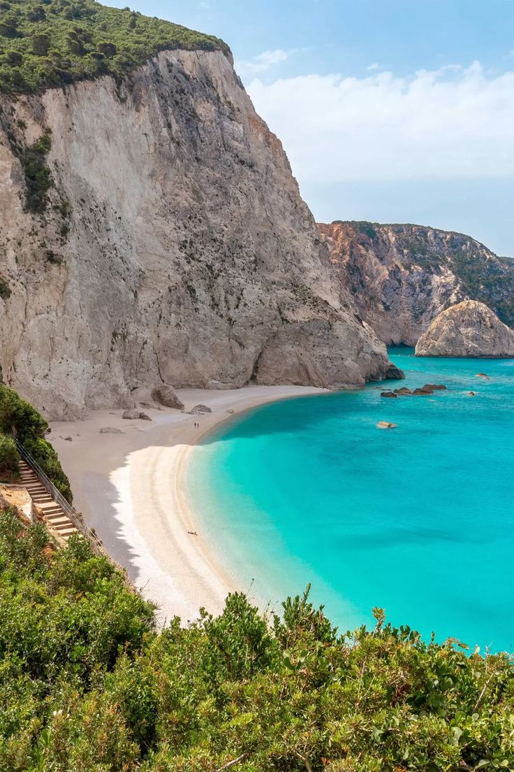 the blue water and white sand beach is surrounded by green trees, bushes and cliffs