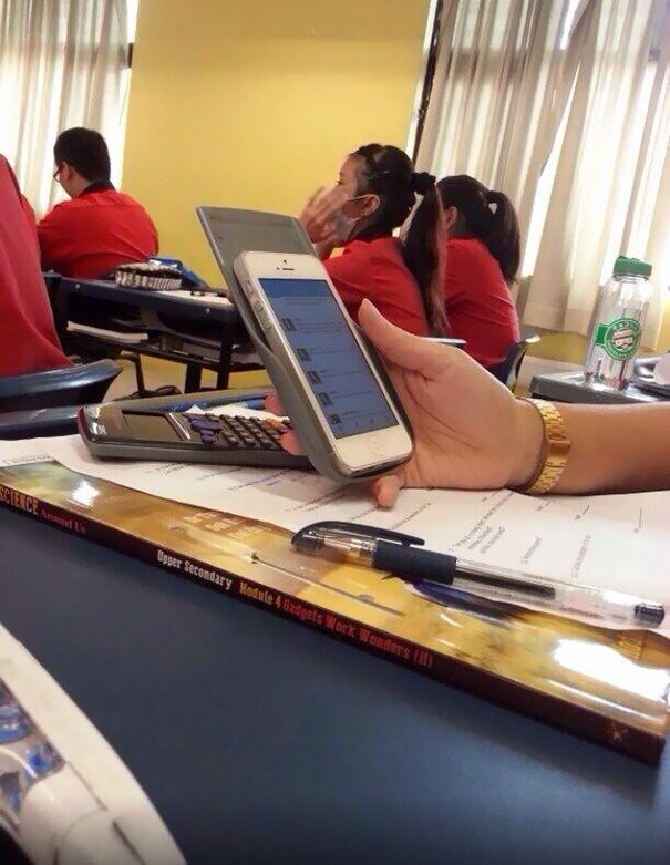 two people sitting at desks with cell phones and papers in front of their faces