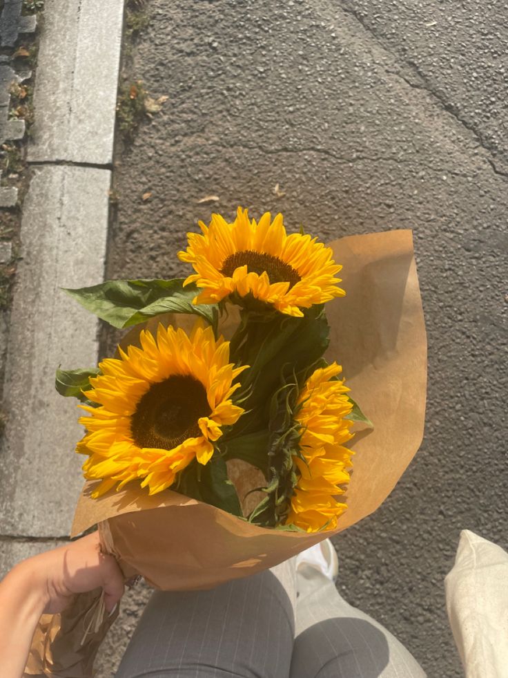 a person holding a bouquet of sunflowers in their hand while sitting on the sidewalk