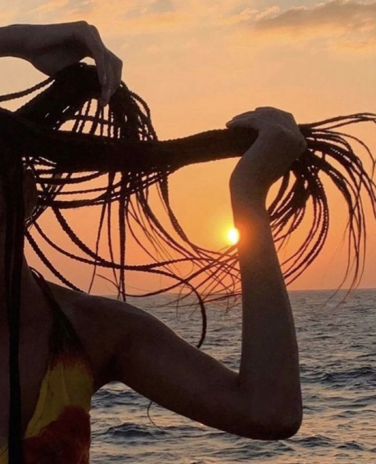 a woman standing on the beach with her hair blowing in the wind and sun setting behind her