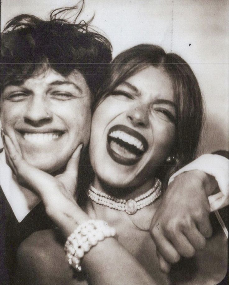 an old photo of two people laughing and posing for the camera with their hands on each other's shoulders