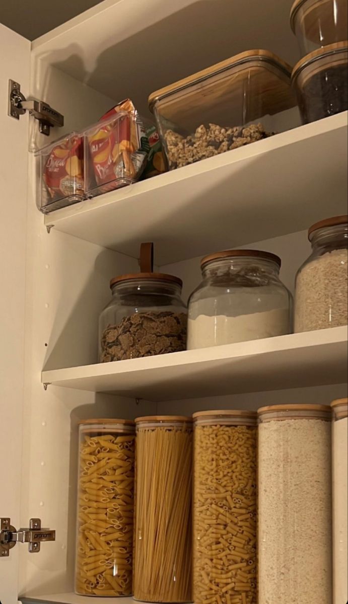 an organized pantry with lots of food in glass jars and cereals on the shelves