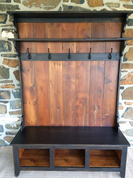 an old wooden bench with metal hooks on the back and shelf below it, in front of a stone wall