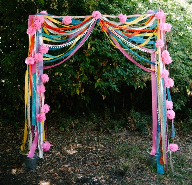 an outdoor wedding arch decorated with streamers and pom poms