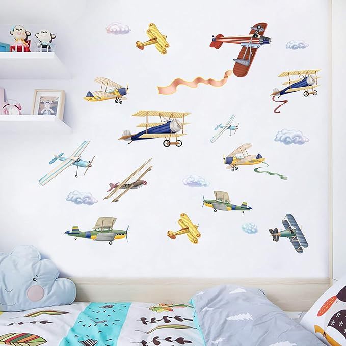 a child's bedroom with an airplane wall decal on the wall and various airplanes flying in the sky