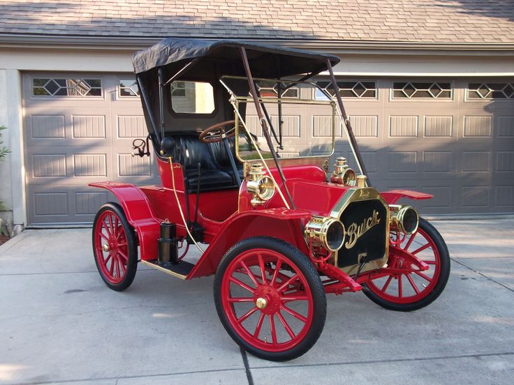 an old fashioned red car parked in front of a house with garage doors and windows