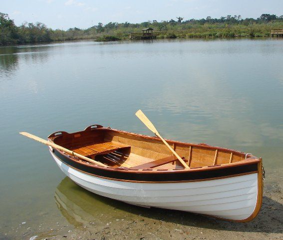 a small wooden boat on the shore of a lake with two oars sticking out of it