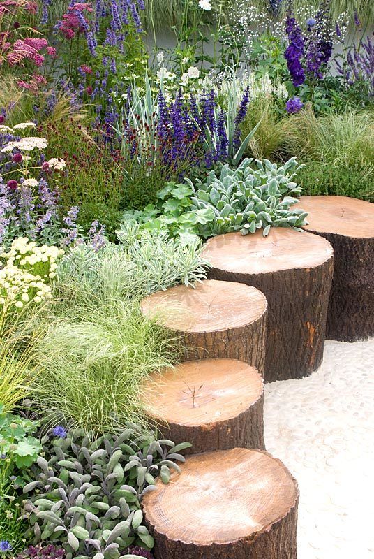 several wooden logs sitting in the middle of a garden filled with flowers and greenery