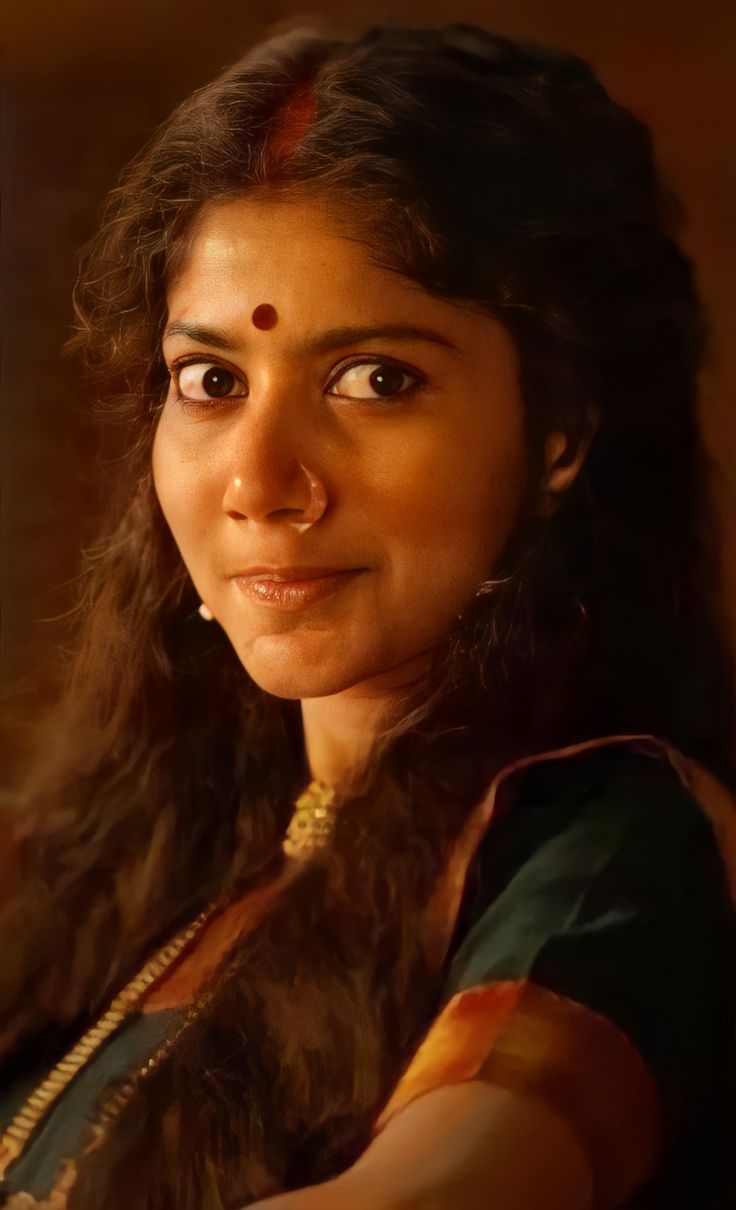 a woman with long dark hair wearing a green sari and gold necklace looking at the camera