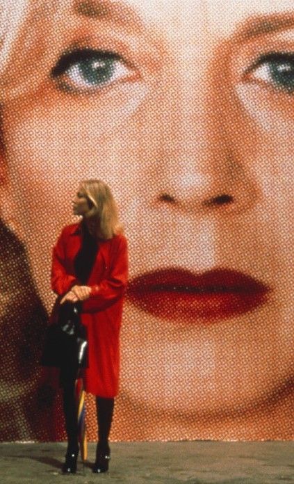 a woman is standing in front of a large portrait of blond haired woman with blue eyes