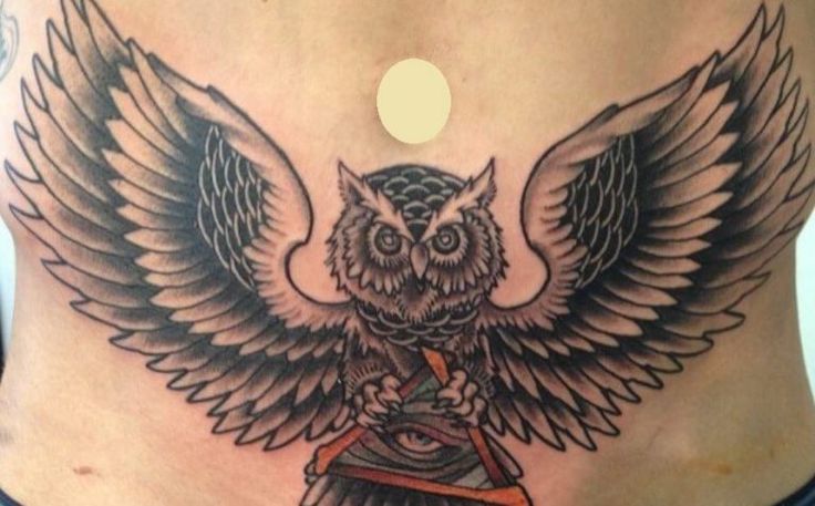 an owl tattoo on the side of a woman's stomach, with wings spread out