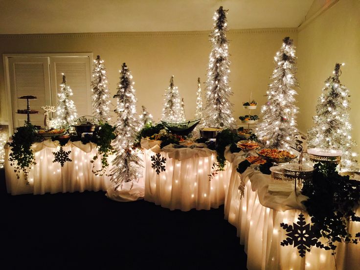 christmas trees are lined up on tables with white lights