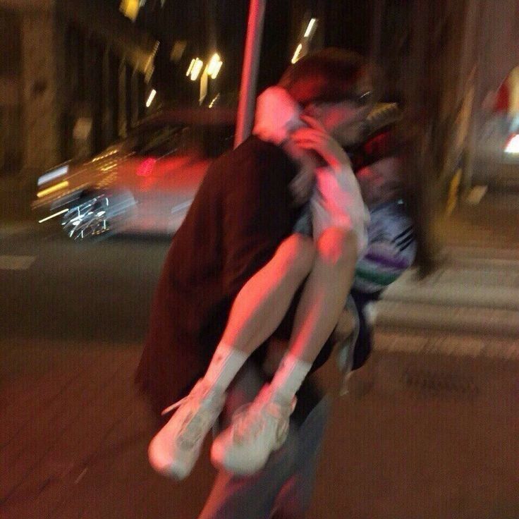 two people are hugging on the street corner at night, one person is holding his head