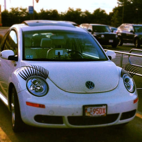 a white beetle parked on the side of a road next to a parking lot with lots of cars behind it