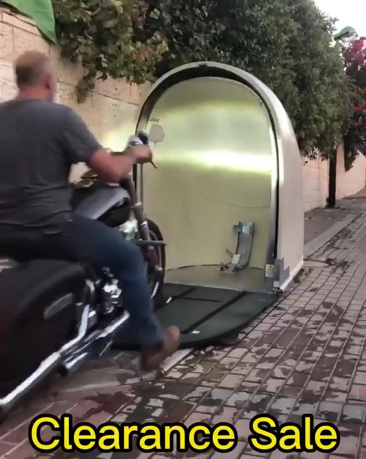 a man riding on the back of a motorcycle next to a brick wall and trees