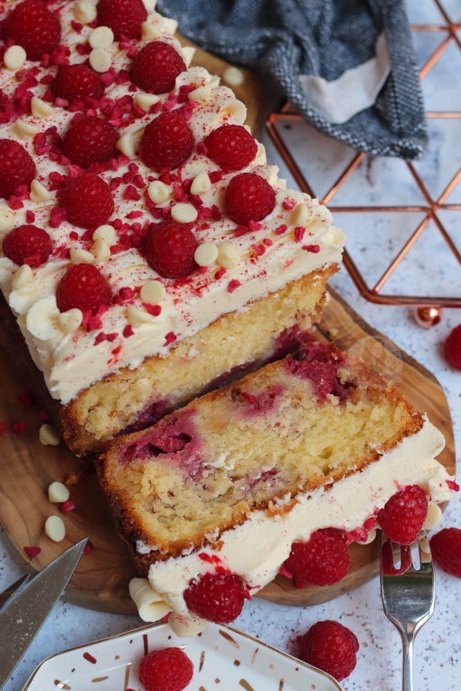 two slices of cake with raspberries and white frosting on a cutting board