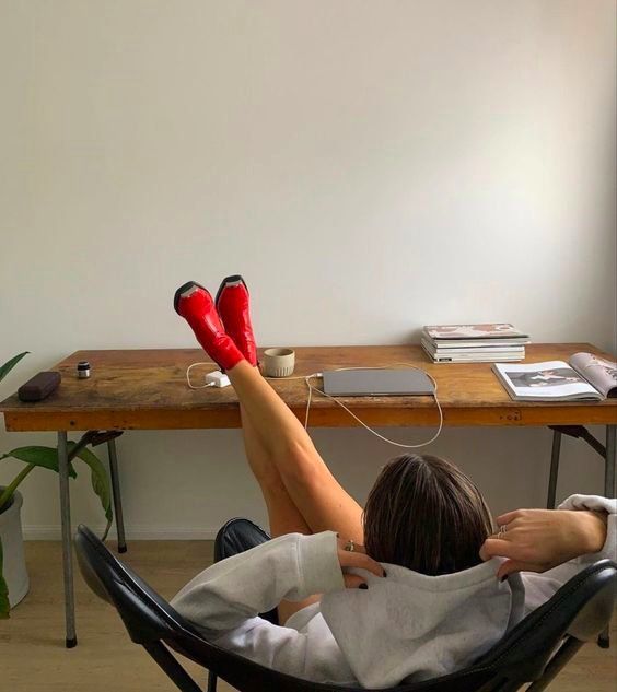 a woman sitting in a chair with her feet up on a desk and wearing red shoes